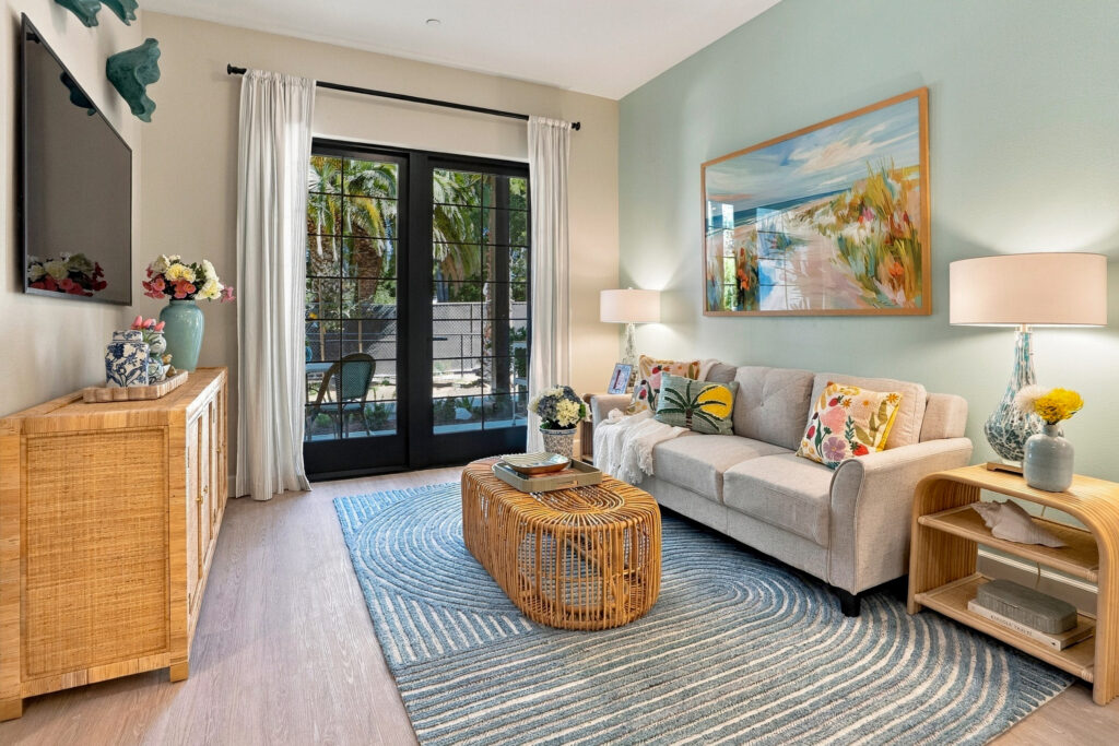 Living space with a sofa and TV, bright pastel decor, and a full glass door out to a terrace