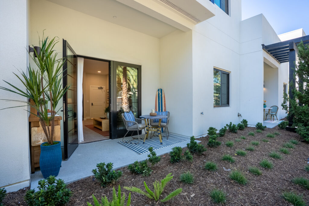 Exterior view of a private terrace with the door open, a table and two chairs, and new plans surrounding it.
