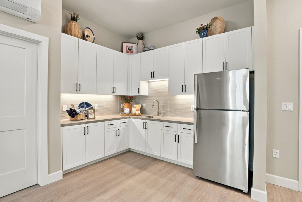 Corner kitchen space with white cabinets, under-cabinet lights, and a stainless steel refrigerator