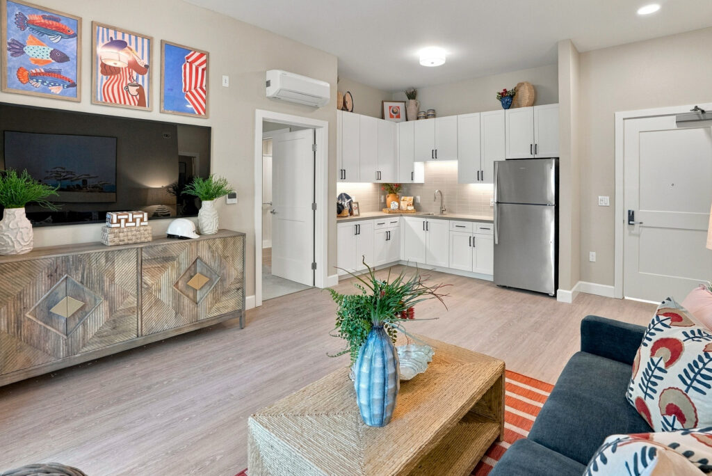 View of living space from the sofa, looking toward a TV, the entrance to bed and bath, and a corner kitchen.
