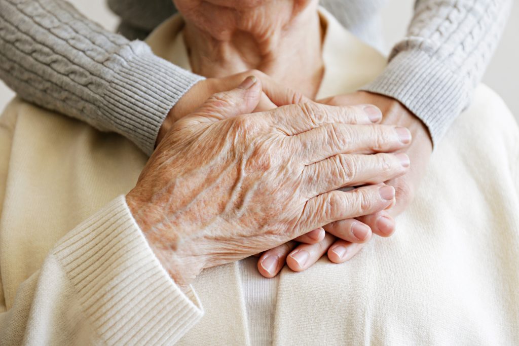 a resident's hand is covering the two hands of someone behind them who has their arms around them