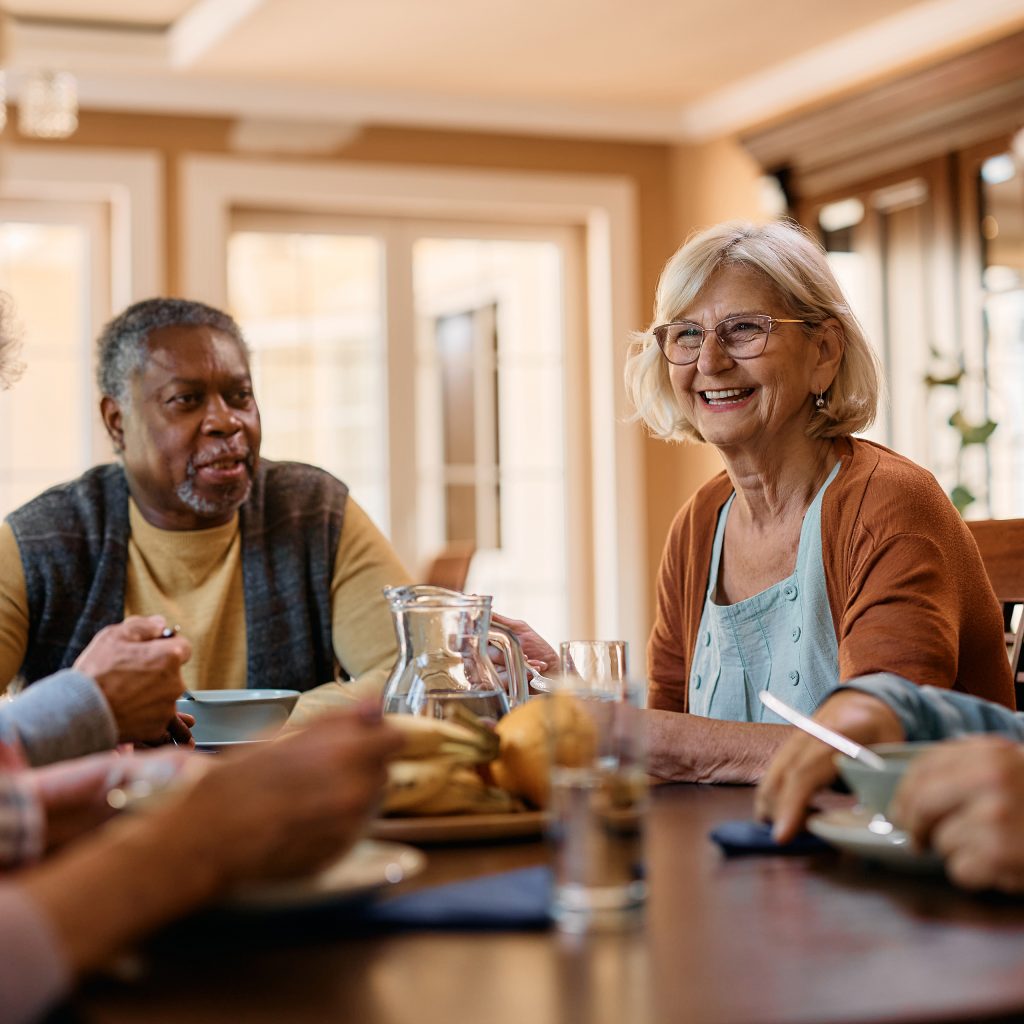 five residents sit around a table indoors, sharing a conversation over a meal