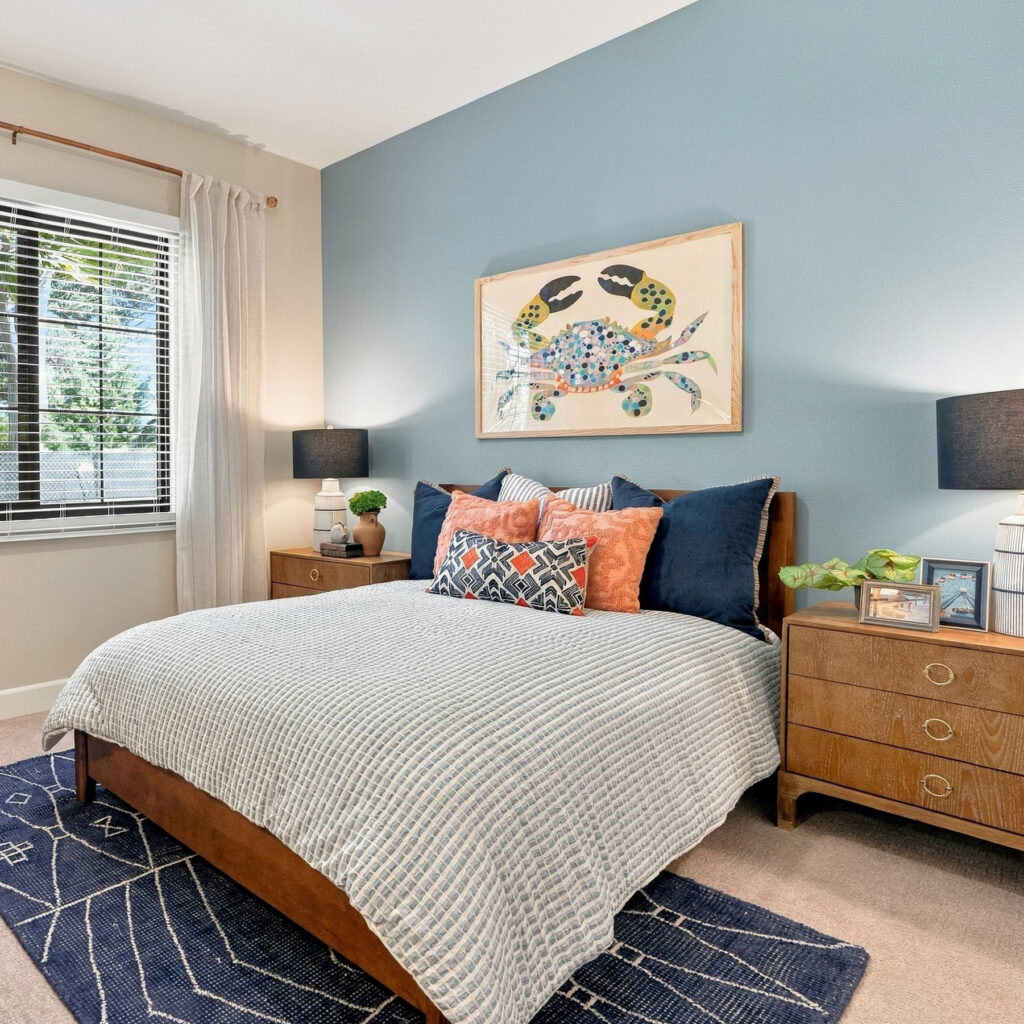 Bedroom space with blue and orange decor, end tables with lamps, and a window looking outside.